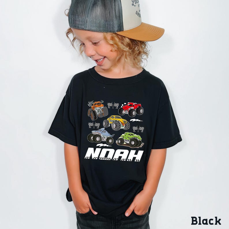 A young boy wearing a black t-shirt with a graphic of monster trucks and the name "Noah" printed on it.