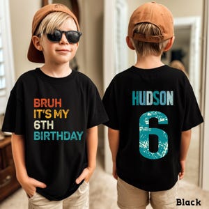 May include: Black t-shirt with the text "BRUH IT'S MY 6TH BIRTHDAY" in red, yellow, and blue. The back of the shirt has the name "HUDSON" and the number "6" in blue. The shirt is worn by a child wearing a brown baseball cap and sunglasses.