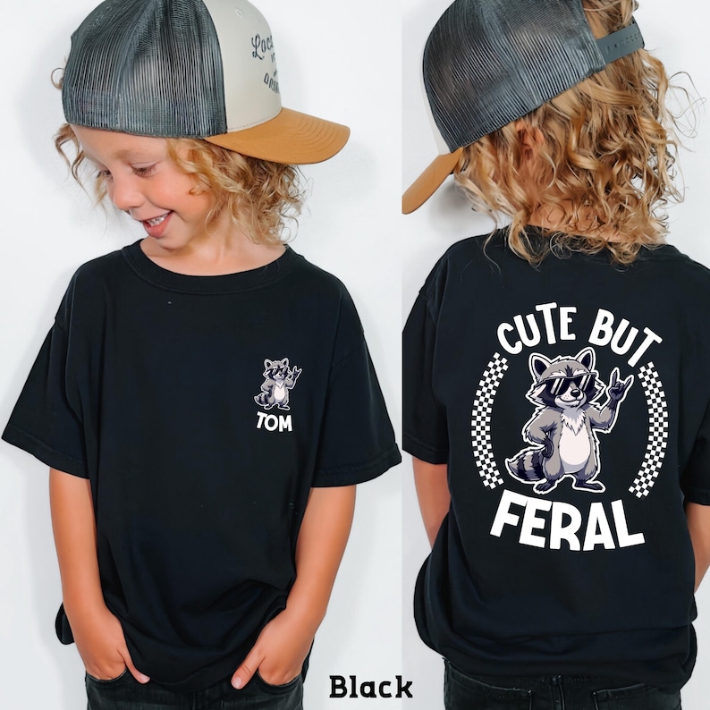 A young boy wearing a black t-shirt with a graphic of a raccoon and the text "CUTE BUT FERAL" printed on the back.