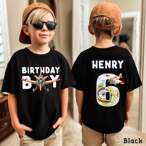 A young boy wearing a black t-shirt with a birthday message and an airplane graphic, and the number 6 on the back.