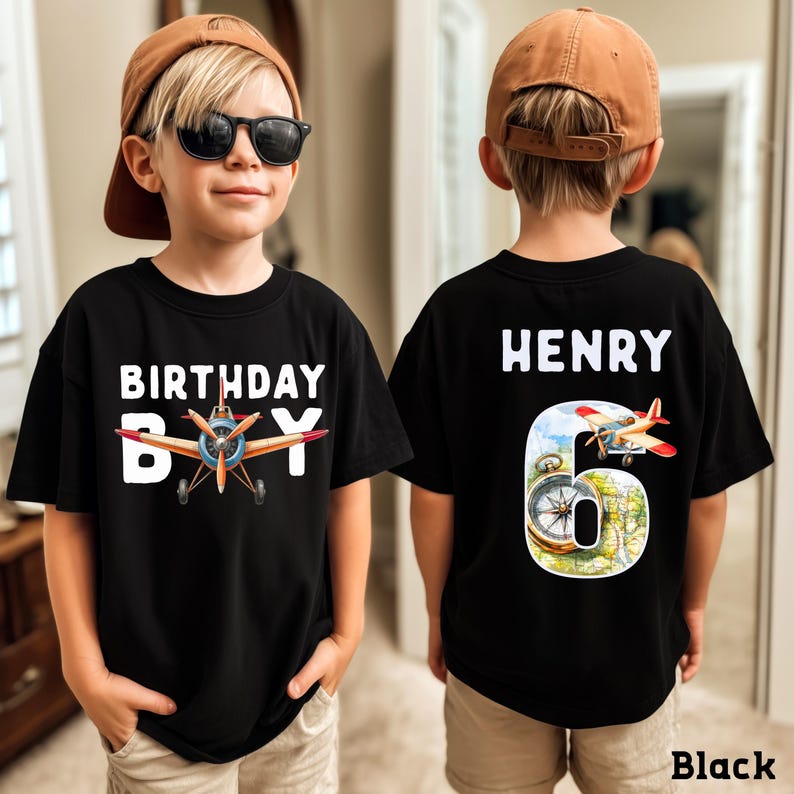 A young boy wearing a black t-shirt with a birthday message and an airplane graphic, and the number 6 on the back.