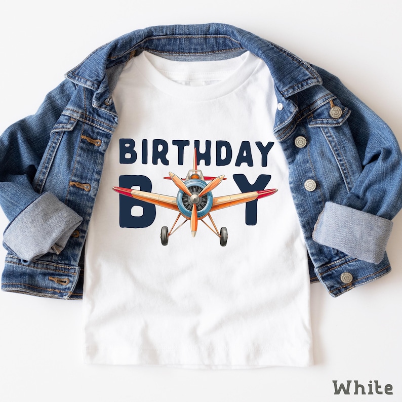 A white t-shirt with a graphic of a propeller plane and the text "BIRTHDAY BOY" printed on it, along with a denim jacket.