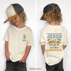 Personalized Jesus Lemonade Shirt with happy lemon graphics and the quote “Life Gave Me Some Lemons, But My Jesus He Be Makin’ Lemonade” — cute faith based kids sweatshirt and Christian shirt.