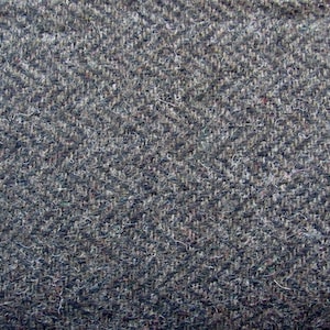 May include: A close-up view of a woven fabric featuring a dark gray and charcoal herringbone pattern. The material has a textured, slightly fuzzy surface with visible interlacing threads that create a repeating V-shaped zigzag design throughout.