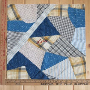 May include: A patchwork quilt square with various fabric patterns in blue, white, yellow, and gray. The word "Lois" is embroidered in red thread. The quilt is approximately 10 inches square.