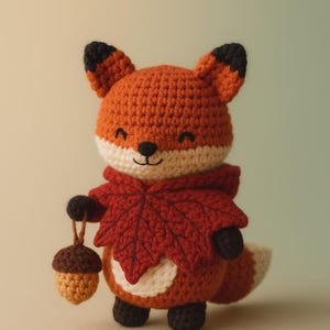 May include: A crocheted fox doll with orange fur, black ears, and a white face and belly. It wears a red leaf-shaped scarf and holds a brown acorn. The fox has a smiling expression and is a charming handmade item.
