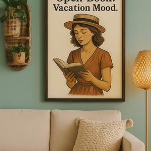 May include: A framed print with the text "Open Book. Vacation Mood." depicts a woman in a hat reading a book. The artwork is in a dark brown frame, hanging above a beige sofa with a textured pillow.