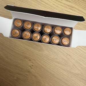 Puede incluir: Una caja de cartón rectangular blanca que contiene doce tubos cilíndricos dispuestos en dos filas. Cada tubo tiene una tapa de color tostado claro con el número 644 impreso en tinta negra en la parte superior. La caja está abierta.
