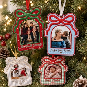 May include: Four custom photo ornaments shaped like gift boxes with bows. One is red with The Smith Family 2026, one is light blue with I Love You, Nana!, one is beige striped with Milo & Luna 2026, and one is green plaid with Baby Sophia 2026.