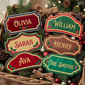 May include: Six rectangular and arched decorative name plaques with scalloped edges, featuring embroidered names Olivia, William, Sarah, Henry, Ava, and The Smiths. Each plaque displays holly berry accents and gold-coloured lettering.
