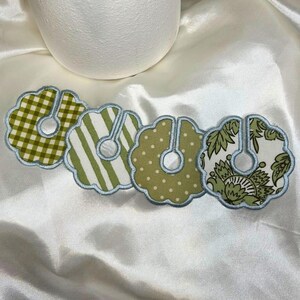May include: Four decorative fabric coasters with a scalloped edge and a light blue trim. Each coaster features a different pattern: green gingham, green stripes, green polka dots, and a green floral design.