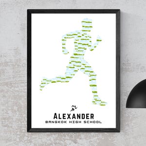 May include: Framed print featuring a running figure composed of green and blue brushstrokes on a white background. The name "ALEXANDER" and "BANGKOK HIGH SCHOOL" are printed in black below the runner silhouette. The frame is black.