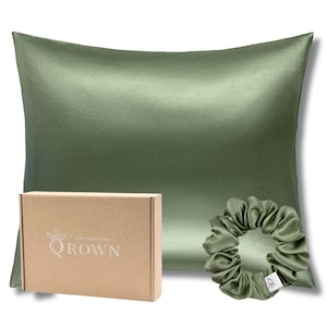Peut inclure: Un oreiller en soie vert olive, une chouchou assortie et une boîte en carton. L'oreiller rectangulaire a une surface lisse et brillante. La chouchou est ronde et froncée. La boîte porte l'inscription "QROWN silk collection".