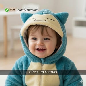 May include: A baby wearing a blue and cream-colored hooded jumpsuit with a zipper closure. The jumpsuit has a cartoon character design with ears on the hood. The text "High-Quality Material" and "Close up Details" are visible.