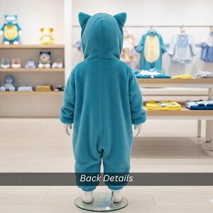 May include: A teal blue hooded jumpsuit for children, featuring cat-like ears on the hood. The outfit is displayed on a mannequin in a children's clothing store. The text "Back Details" is visible at the bottom of the image.