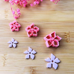 Peut inclure: Emporte-pièces en forme de fleurs roses et lavande sur une surface en bois. Les emporte-pièces sont de différentes tailles et modèles, certains ayant un effet de pétales superposés. Fleurs roses et accents floraux roses en arrière-plan.