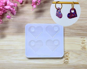 May include: A clear silicone mould featuring four heart-shaped cavities, each with a small hole at the top. Two heart-shaped earrings with glittery red, blue, and purple accents are shown on a gold hoop. The text "TYLIAFCO" is at the bottom.