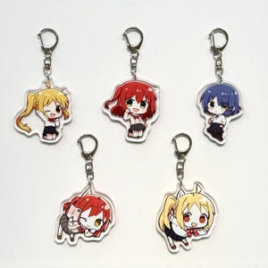 Puede incluir: Cinco llaveros de personajes de estilo anime. Cada llavero presenta un personaje diferente con un color y estilo de cabello únicos, vistiendo un uniforme escolar. Los llaveros son de acrílico transparente y tienen llaveros plateados.