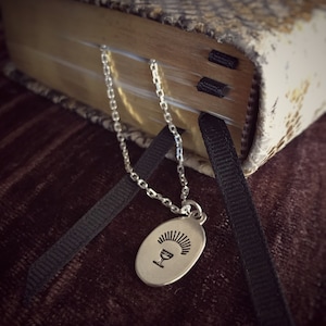 Puede incluir: Un collar de cadena de plata con un colgante ovalado que presenta una imagen estilizada de un cáliz con un diseño de rayos de sol.