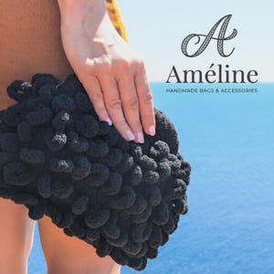 May include: A black clutch bag with a thick, textured, looped yarn surface. The text "A Améline HANDMADE BAGS & ACCESSORIES" is printed in the upper right corner. The bag is held against a background of a blue sea and clear sky.