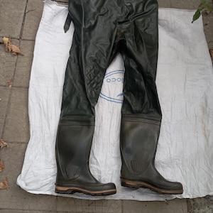 Puede incluir: Un par de vadeadores impermeables de color verde oliva con botas de goma integradas, suelas texturizadas y rodillas reforzadas. El vadeador incluye tirantes ajustables en la parte superior y una construcción de material flexible.