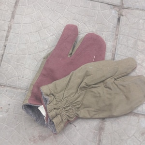 Puede incluir: Un par de guantes de dedo dividido con palma color granate y dorso de lona color canela. Los guantes tienen una sección de muñeca elástica fruncida y un forro interior gris. El diseño separa el pulgar y el índice de los otros tres dedos.