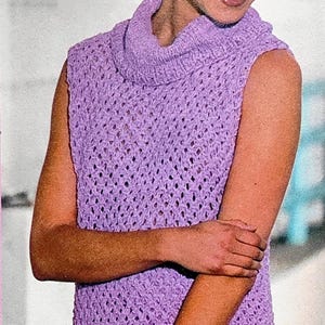 May include: A sleeveless, lilac crochet dress with a cowl neck. The dress has a textured, open weave design. The model is wearing the dress and has their arms crossed.