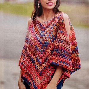 May include: A colorful, open-shoulder crochet poncho in shades of red, orange, blue, and pink. The handmade garment features a square pattern design. The poncho is a unique, bohemian-style accessory.