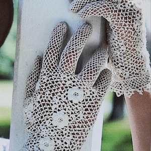 May include: A pair of off-white, open-weave crochet gloves. The gloves feature a floral design on the back of the hand and a scalloped edge at the wrist. The crochet pattern creates a delicate, lacy appearance.