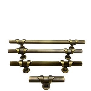 May include: Antique brass cabinet pulls in various sizes. The pulls have a ribbed, cylindrical design with decorative end pieces and circular bases. The hardware is displayed against a white background.