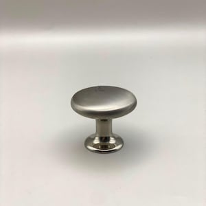 May include: A brushed nickel cabinet knob with a round top and a short, cylindrical base. The knob has a simple, modern design and is suitable for drawers and cabinets. The image is set against a white background.