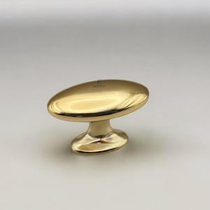 May include: A gold-colored cabinet knob with an oval top and a rounded base. The knob has a shiny, reflective surface. The word "KULPERA" is printed on the top of the knob.