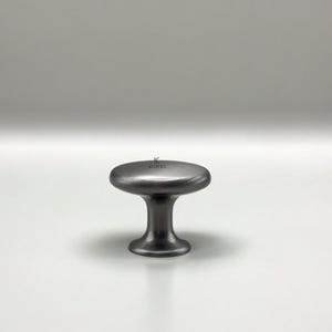 Può includere: Un pomello per armadio grigio scuro con una parte superiore arrotondata e una base corta e cilindrica. Il pomello ha una finitura opaca ed è centrato su uno sfondo bianco. Il marchio "KUPPER" è stampato sulla parte superiore del pomello.