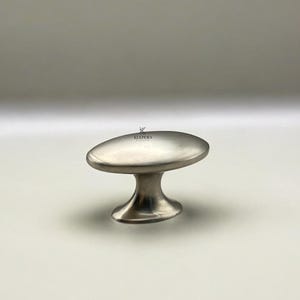 Può includere: Pomello per mobili in nichel spazzolato con parte superiore ovale e base curva. Il pomello è un design moderno, adatto per cassetti o ante di armadi. Il marchio "KULPERA" è stampato in alto.