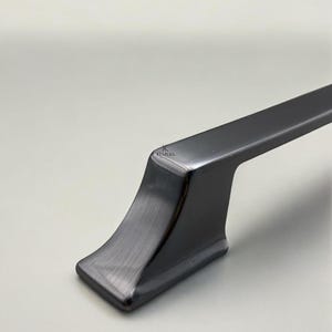 May include: Close-up of a dark gray cabinet pull with a rectangular handle and a flared base. The hardware has a brushed metal finish and a modern design. The brand name "KLURA" is subtly visible.