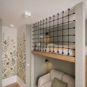 Könnte beinhalten: Eine Hochbettplattform verfügt über eine Sicherheitsnetzbarriere aus schwarzem Seil, die an der Decke befestigt ist. Das Bett hat weiße Bettwäsche und befindet sich über einem hellen Sofa. Die Wände sind mit einer botanischen Tapete gestaltet.