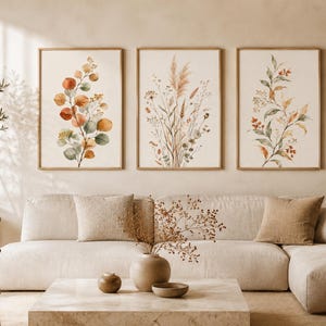 Può includere: Un set di tre stampe da parete incorniciate con illustrazioni ad acquerello di elementi botanici. La stampa a sinistra mostra foglie di eucalipto arancioni e verdi, quella centrale erbe alte e quella a destra delicati rami frondosi.