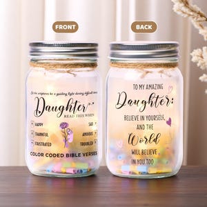 May include: Two glass mason jars with silver lids, each wrapped with twine. The front jar reads "Daughter" and "Color Coded Bible Verses." The back jar says "To My Amazing Daughter." Both jars are filled with colorful paper scrolls.