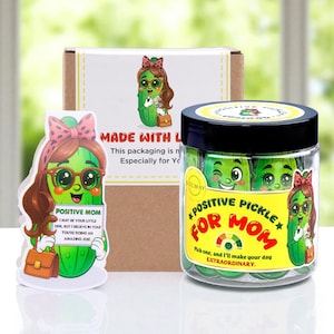 May include: A gift set featuring a jar of green candies labeled "Positive Pickle for Mom," a card with a pickle character, and a box. The jar has a black lid and a yellow label. The card reads "Positive Mom."