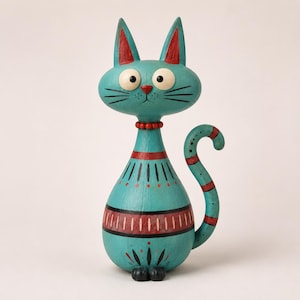 Puede incluir: Una figura de gato color cerceta con grandes ojos blancos, una pequeña nariz roja y bigotes negros. El cuerpo presenta patrones pintados en rojo y negro, incluyendo bandas horizontales, rayas verticales y puntos.