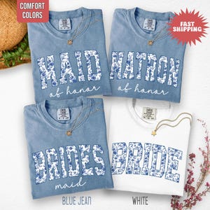 May include: Four t-shirts with text for a bridal party. Three are blue with "MAID of honor", "MATRON of honor", and "BRIDES maid" in white floral letters. The fourth is white with "BRIDE" in blue floral letters.
