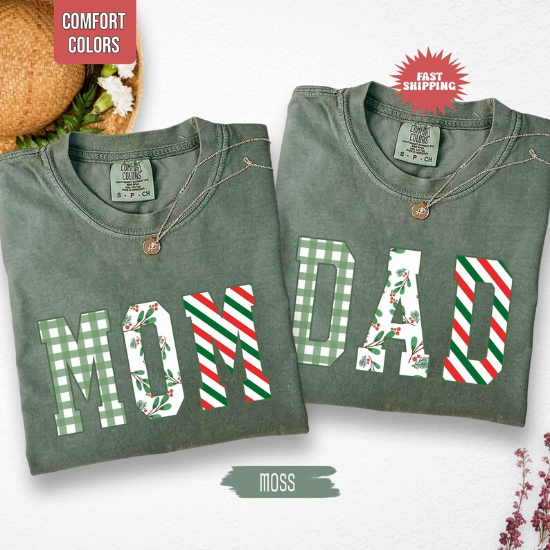 May include: Two moss green t-shirts with the words "MOM" and "DAD" in a mix of green plaid, red and white stripes, and floral patterns. Each shirt has a Comfort Colors tag and a necklace. The image also includes the text "MOSS".
