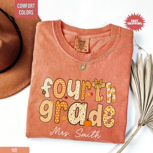 May include: A peach-colored Fourth Grade teacher t-shirt with the text "Fourth Grade Mrs. Smith" in a fall-themed design. The design includes pumpkins, leaves, and plaid patterns. A gold necklace and a brown hat are also visible.