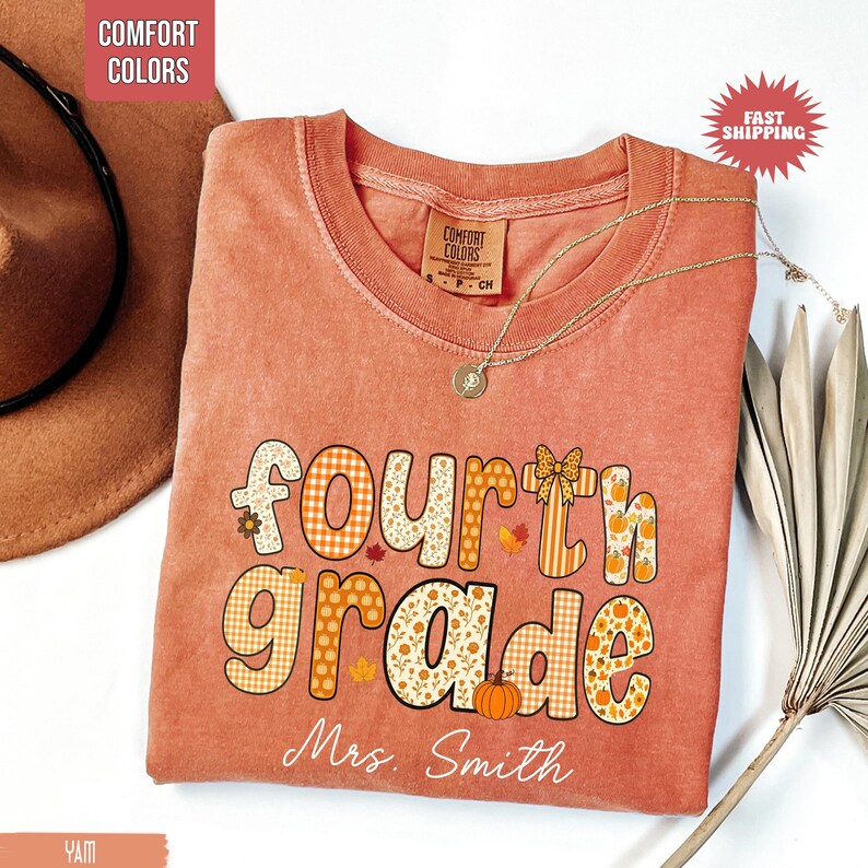 May include: A peach-colored Fourth Grade teacher t-shirt with the text "Fourth Grade Mrs. Smith" in a fall-themed design. The design includes pumpkins, leaves, and plaid patterns. A gold necklace and a brown hat are also visible.