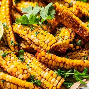 May include: Close-up of grilled corn on the cob, cut into pieces, with visible kernels and a golden-brown exterior. Garnished with fresh green coriander. A delicious and appetizing dish.