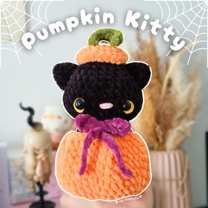 May include: A handmade black cat plushie wearing an orange pumpkin costume with a green stem. The plushie has yellow eyes and a pink nose, and a purple bow. The text "Pumpkin Kitty" is at the top.