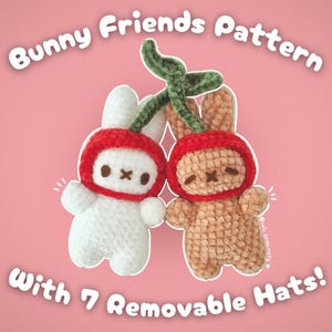 May include: Two crocheted bunny plushies wearing red cherry hats with green stems. The bunnies are white and brown. The text "Bunny Friends Pattern with 7 Removable Hats!" is written on a pink background.