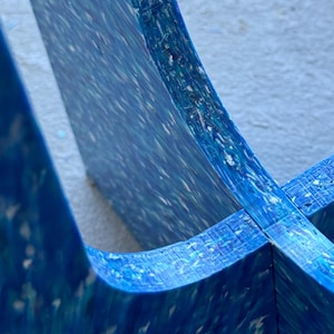May include: Close-up of a section of a blue, multi-layered object with a speckled pattern. The object has a curved shape and appears to be made of a composite material. The color palette includes shades of blue and white.