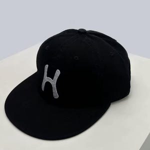 Peut inclure: Casquette de baseball noire avec une visière incurvée et une lettre "H" grise brodée sur le devant. Le chapeau a un bouton sur le dessus. Accessoire classique.