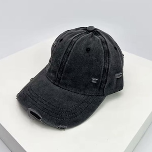 May include: A black, distressed baseball cap with a curved peak. The cap has a worn look with several small holes and a button on top. The hat is made of a soft material, suitable for casual wear.